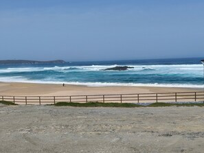Una playa con olas, una persona caminando y una isla distante.