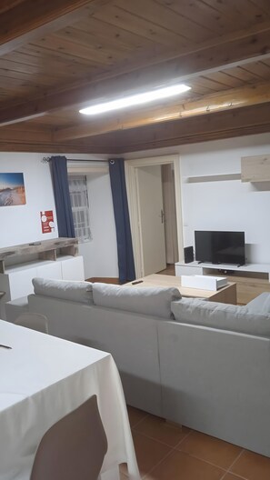 A modern living room with a sofa, a TV, and a dining area with a table.