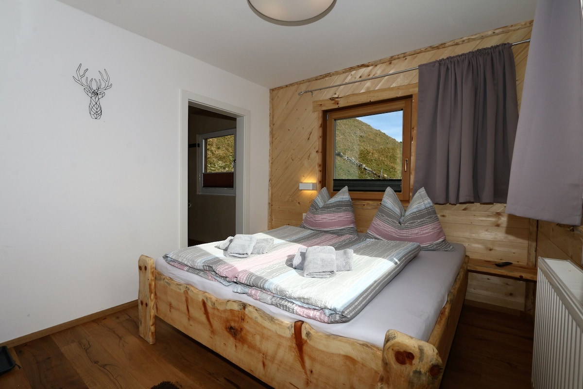 A wooden bed with a view of a mountain, a window with curtains, and a wall with a deer head decoration.