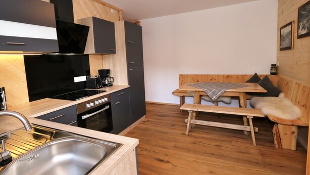 A compact kitchen with modern appliances, a dining area with a bench, and a wooden wall. - Unique Alpine Pasture in the Zillertal Mountains (Zellberg)