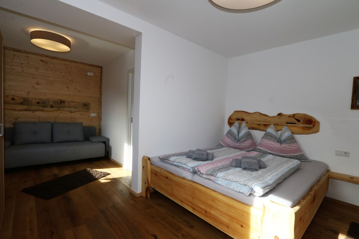 A bedroom with a wooden bed, a gray sofa, and a wooden wall panel.