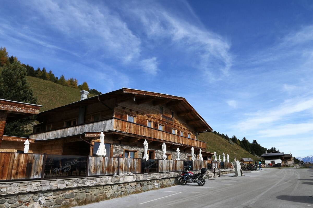 A wooden chalet with balconies, stone walls, and a mountain backdrop.