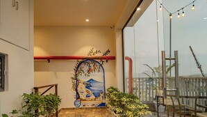 Un pasillo con un mural, plantas en macetas y un balcón con mobiliario exterior.