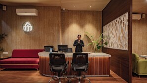 Un área de recepción con pared de madera, un sofá rojo, dos sillas de oficina negras y un sillón verde.