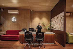 Un área de recepción con pared de madera, un sofá rojo, dos sillas de oficina negras y un sillón verde.