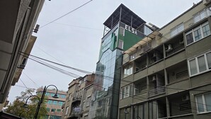 Un edificio de varios pisos con fachada verde y blanca, múltiples balcones y unidades de aire acondicionado.