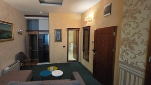 Habitación de hotel con cama, un pequeño rincón de descanso con dos mesas redondas, una puerta y vistas al pasillo.