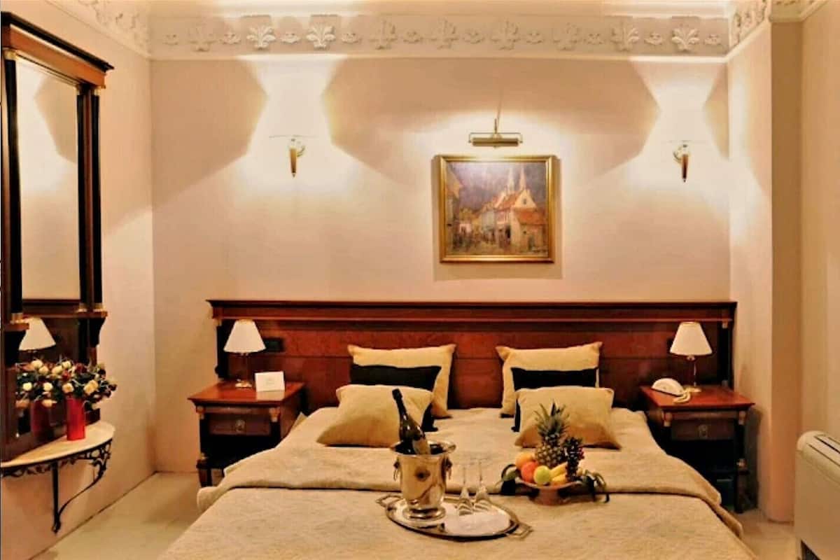 Habitación de hotel con una cama grande, dos mesitas de noche con lámparas, un cuadro en la pared y una cesta de frutas sobre la cama.