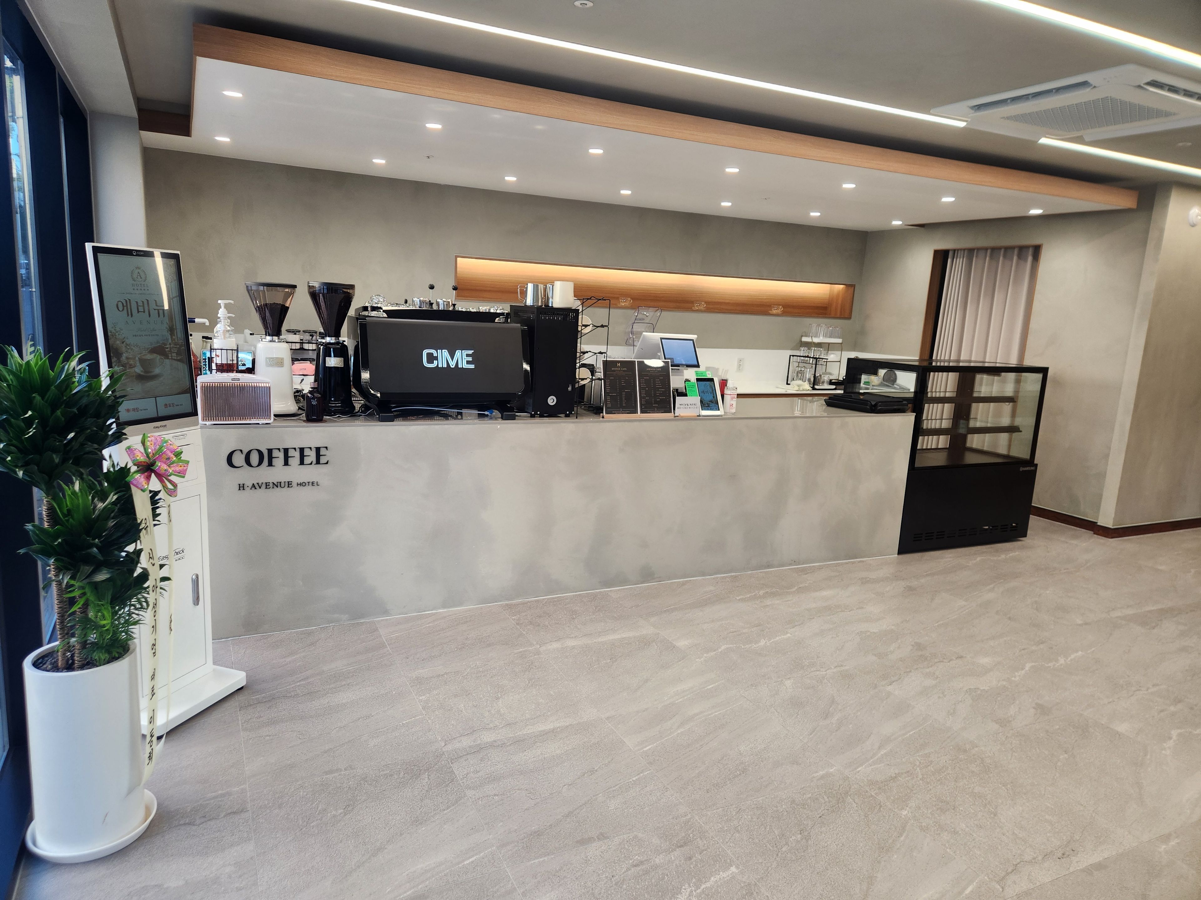 Un espace café moderne doté d’un écran numérique, de machines à café et d’un tableau affichant le menu.