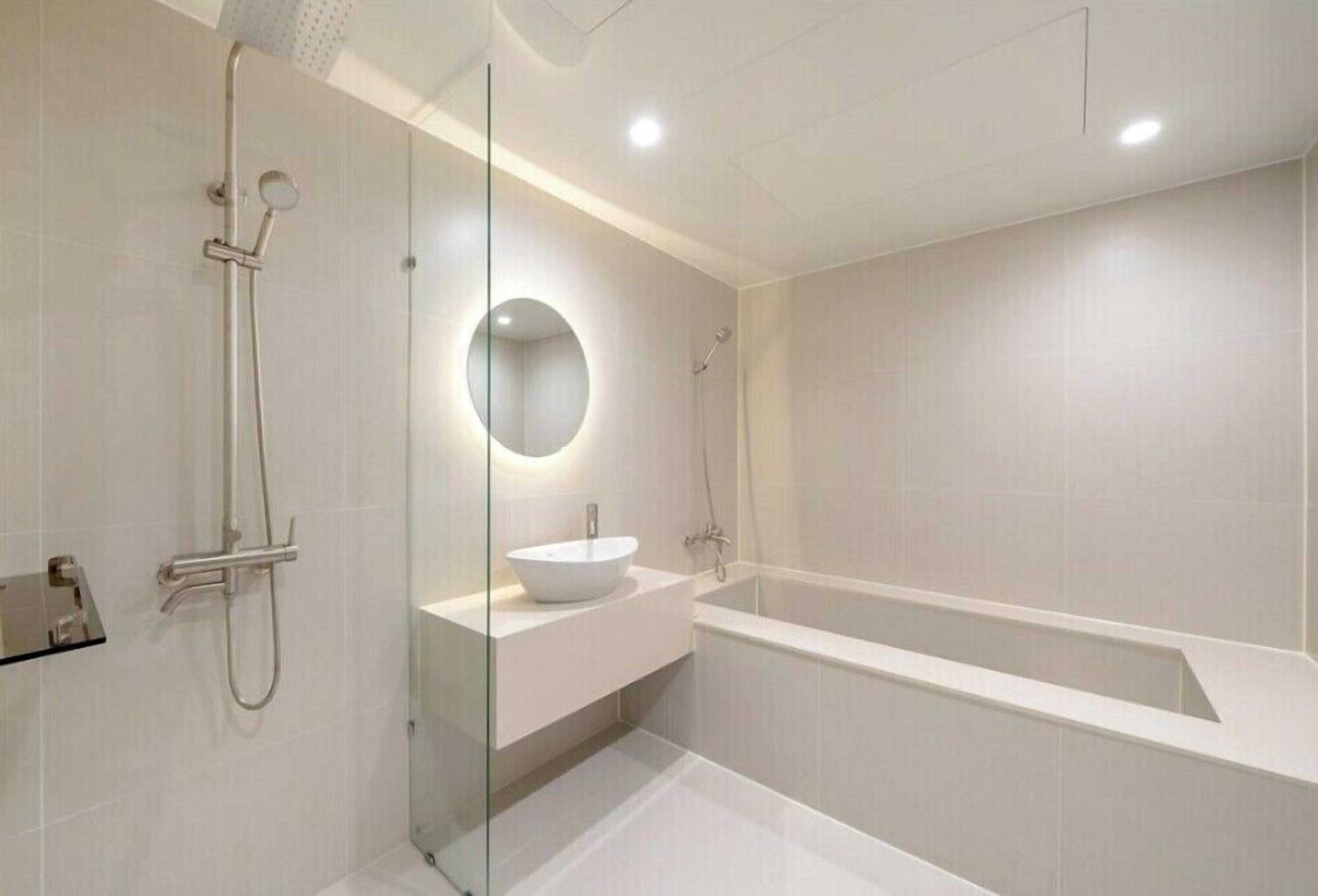 A modern bathroom with a glass-enclosed shower, a round mirror, and a freestanding bathtub.