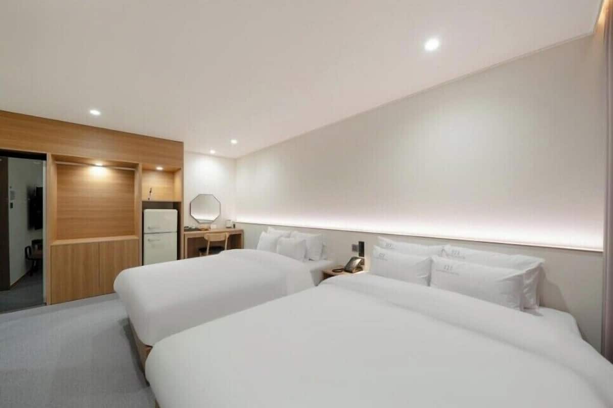 A hotel room with two beds, a desk with a lamp, a mirror, and a wardrobe.