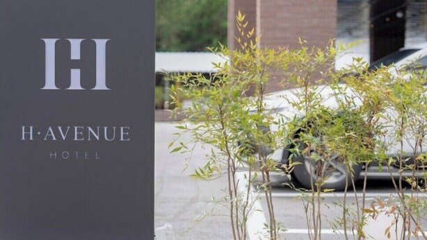 A sign for H·AVENUE HOTEL with a modern building in the background. - H Avenue Hotel Jeonju Terminal (Jeonju)