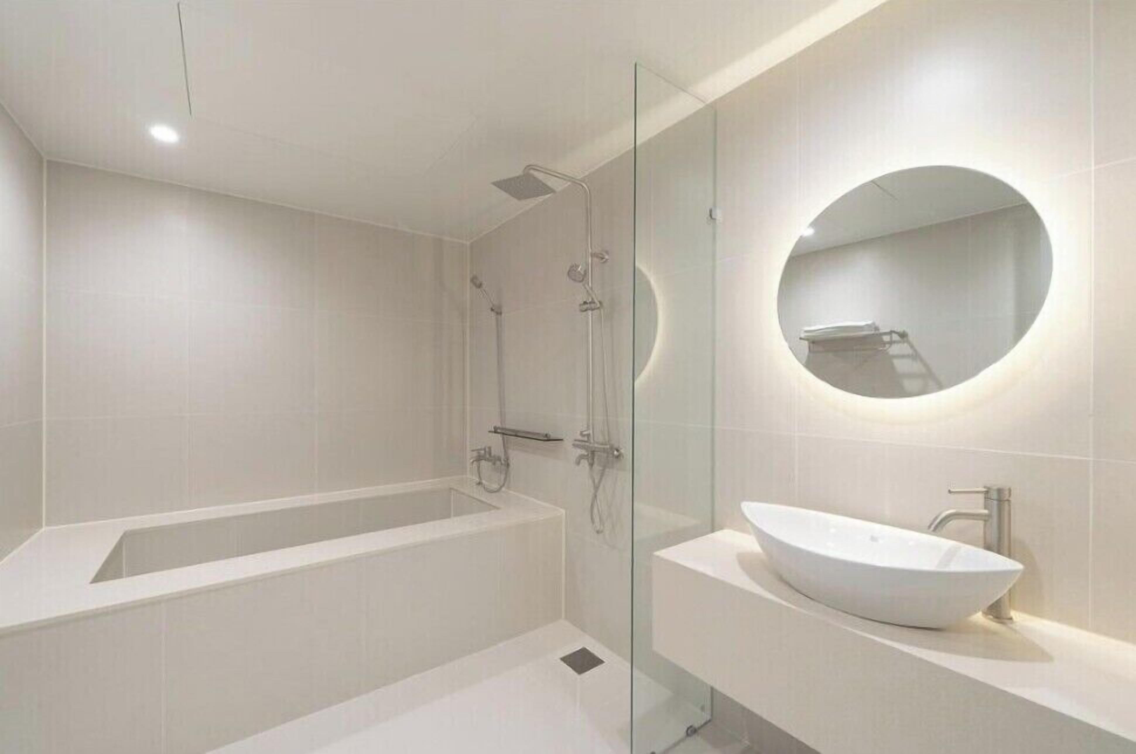 A modern bathroom with a freestanding bathtub, a glass-enclosed shower, and a round mirror above a white sink.