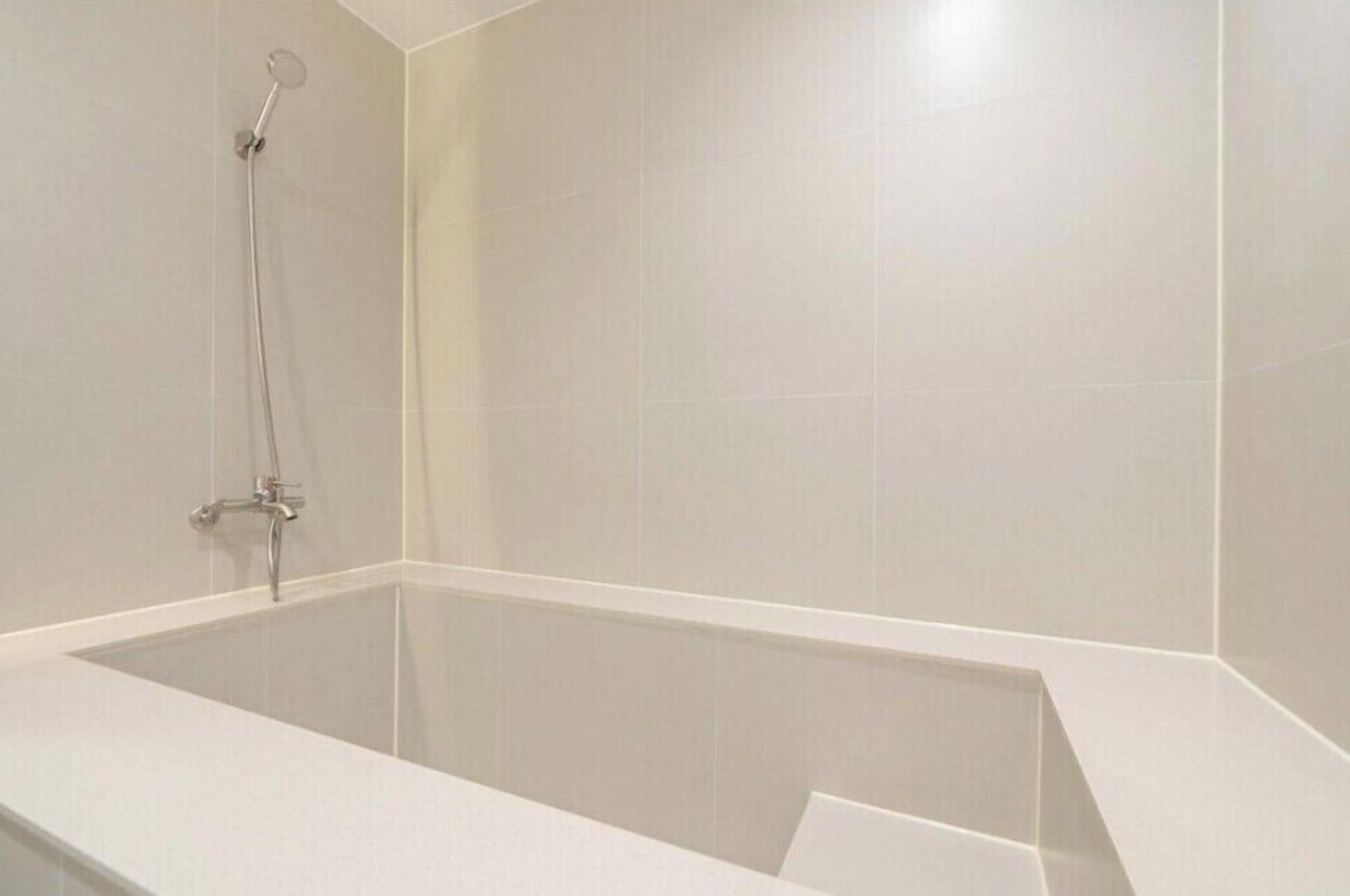 Un baño moderno con una bañera rectangular, un cabezal de ducha manual y un grifo empotrado.