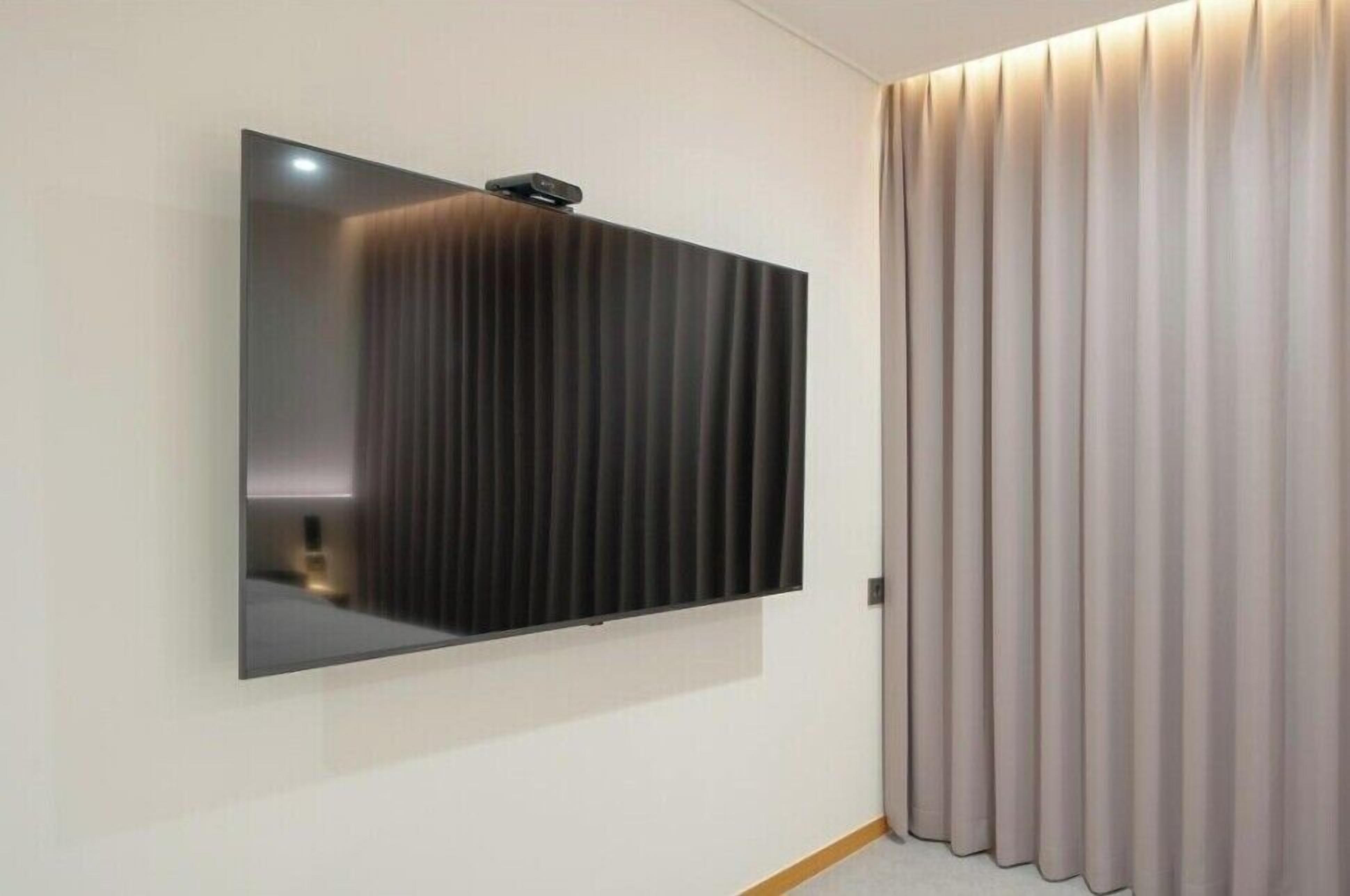Una habitación moderna con un televisor de pantalla plana grande montado en la pared, una puerta corredera con persianas verticales y suelo de madera.