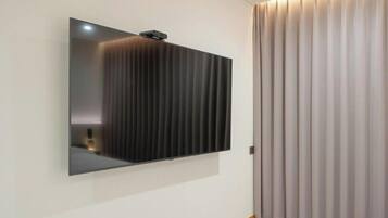 Una habitación moderna con un televisor de pantalla plana grande montado en la pared, una puerta corredera con persianas verticales y suelo de madera.