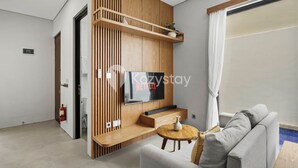 A modern living room with a flat-screen TV, wooden paneling, a grey sofa, and a small round table.
