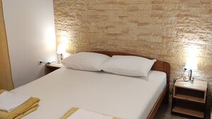 Una cama bien tendida con sábanas blancas y dos toallas amarillas, un cabecero de madera y una pared con textura de piedra.