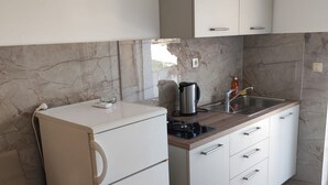 Una cocina compacta con armarios blancos, estufa integrada y salpicadero de mármol.