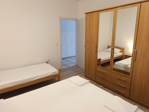 Un dormitorio con dos camas individuales, un armario de madera con espejo y una mesita.