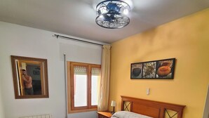 Una camera da letto con un letto, un termosifone, una finestra con tende, uno specchio e una parete con un quadro.