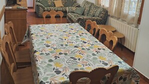 Zona pranzo con tavolo apparecchiato per quattro, divano, televisore e lampadario.