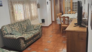Un soggiorno con un divano, un'area pranzo con tavolo e sedie, una televisione e un angolo cottura con frigorifero.