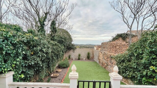 Vista di un giardino con prato verde, muri in pietra e diverse piante.