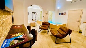 Moderni hotellihuone, jossa on ruokailutila, oleskelualue nahkaisilla tuoleilla, suuri ikkuna ja ovi.