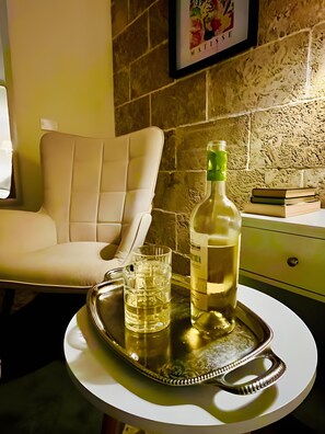 Una habitación con una silla blanca, una bandeja con una botella y un vaso, y un cuadro en la pared.