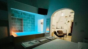 Quarto de hotel com uma cama, área de estar com uma poltrona, televisão fixada na parede e tela de projeção exibindo uma parede com azulejos azuis.
