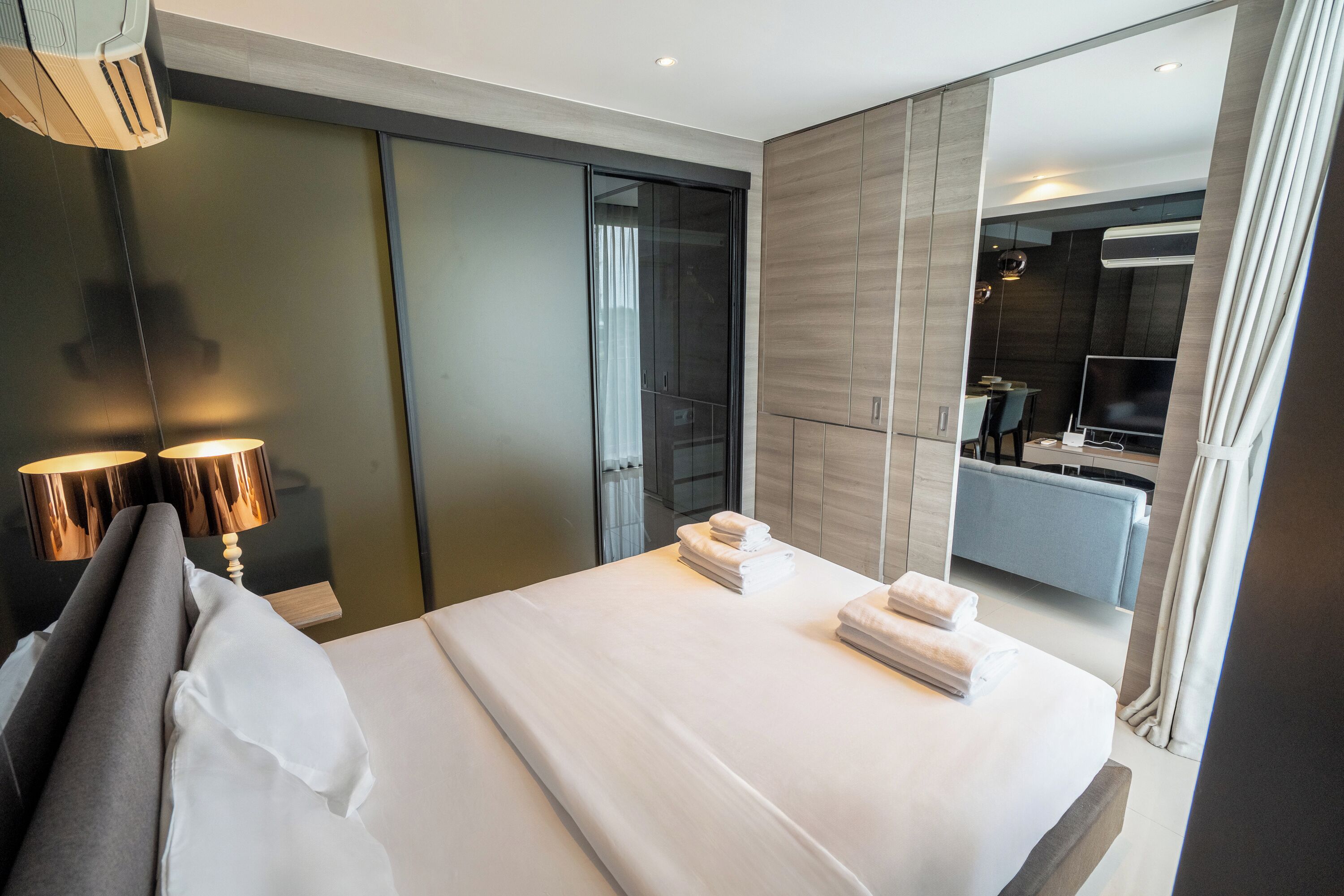 A modern hotel room with a large bed, a bedside lamp, a wardrobe, and a bathroom visible through a sliding door.