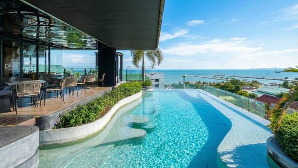 A modern outdoor pool area with a view of the ocean, surrounded by lounge seating and a glass-enclosed bar. - Seaphere residence by Prop Hopper (Sattahip)