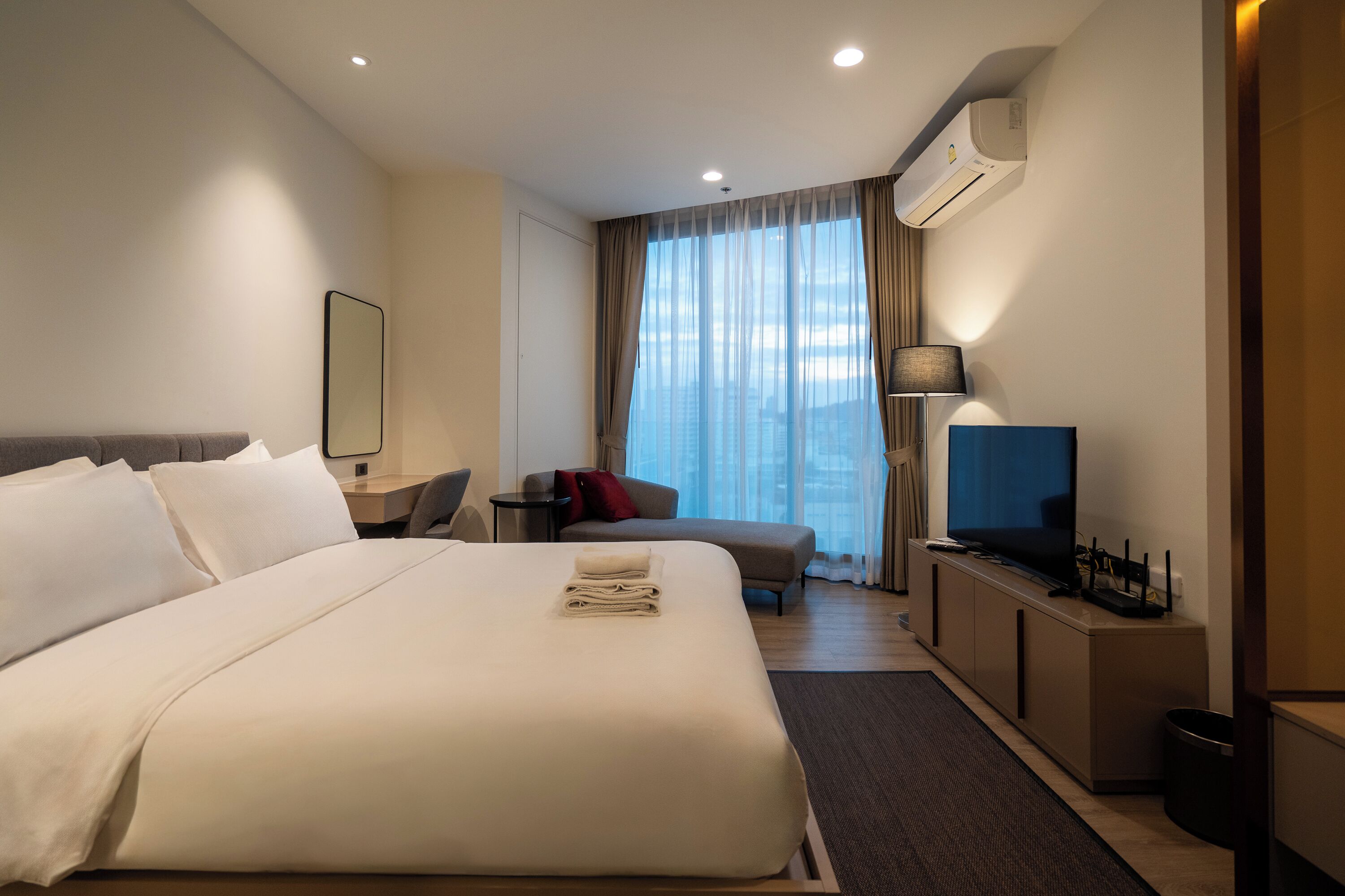 Een hotelkamer met een groot bed, een bureau met computer, een televisie en een raam met gordijnen.
