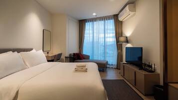 Een hotelkamer met een groot bed, een bureau met computer, een televisie en een raam met gordijnen.