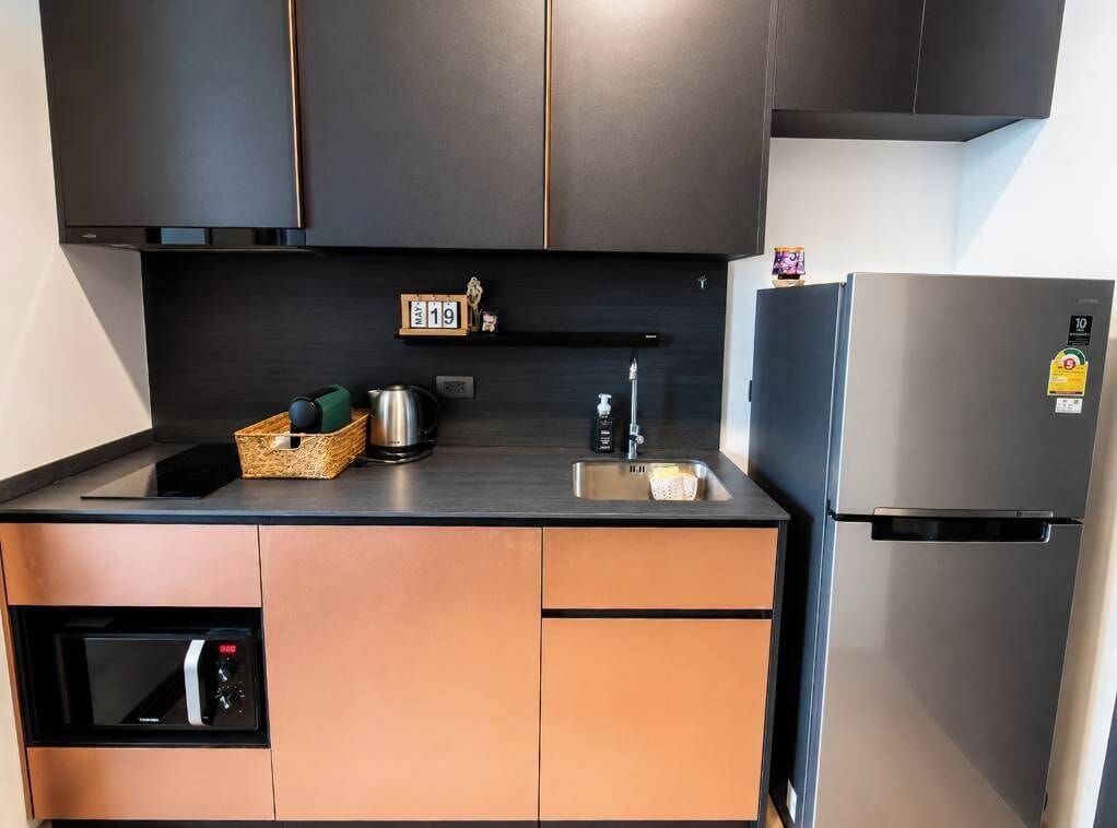 A compact kitchen with a built-in oven, a stainless steel refrigerator, and a small shelf with kitchen items.