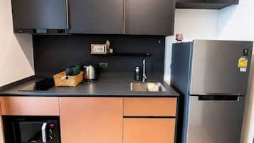 A compact kitchen with a built-in oven, a stainless steel refrigerator, and a small shelf with kitchen items.