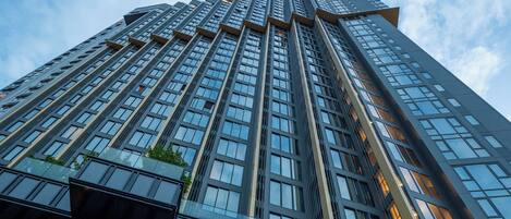 A high-rise building with a modern architectural design, featuring a prominent entrance with glass railings and a well-lit lobby area.