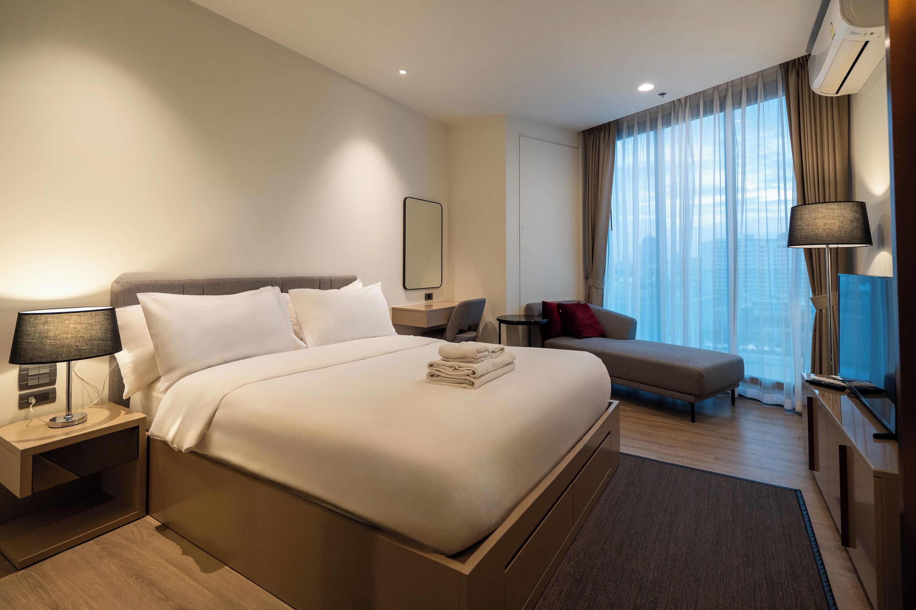 Een moderne hotelkamer met een groot bed, nachtkastjes, een bank, een televisie en uitzicht over de stad.