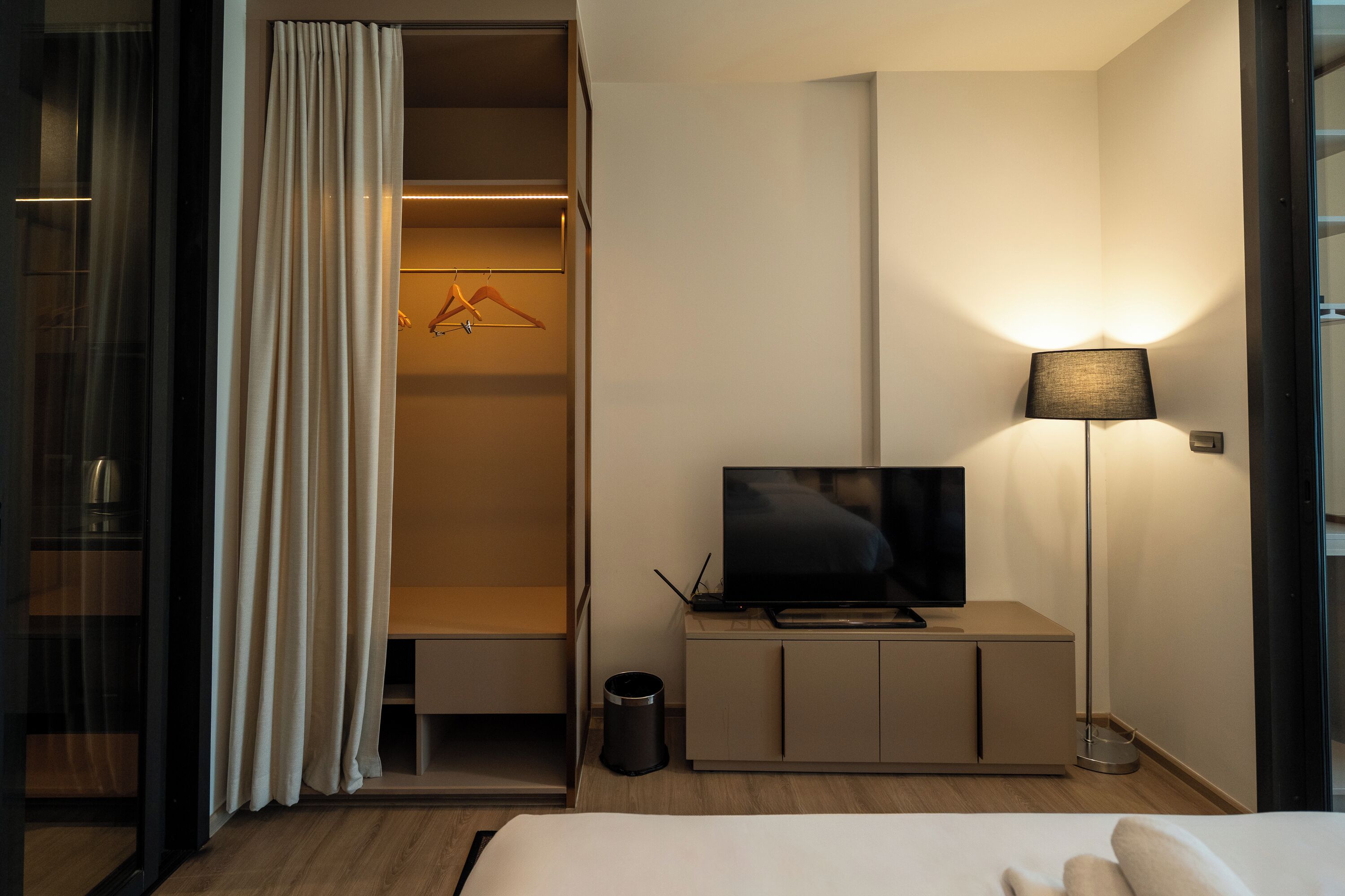 A hotel room with a bed, a TV on a cabinet, a closet with hanging clothes, and a floor lamp.