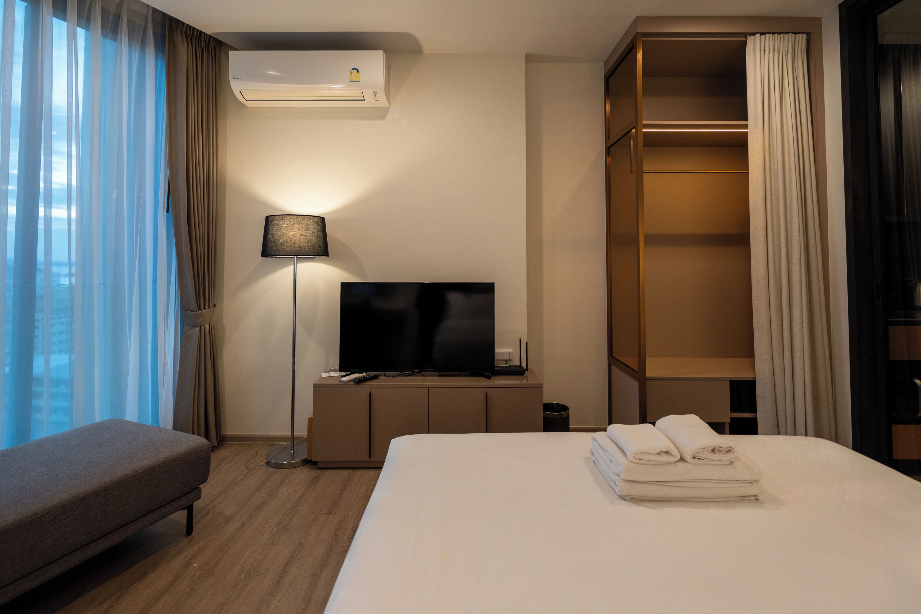 A hotel room with a bed, a TV, a bedside lamp, a wardrobe, and a window with curtains.