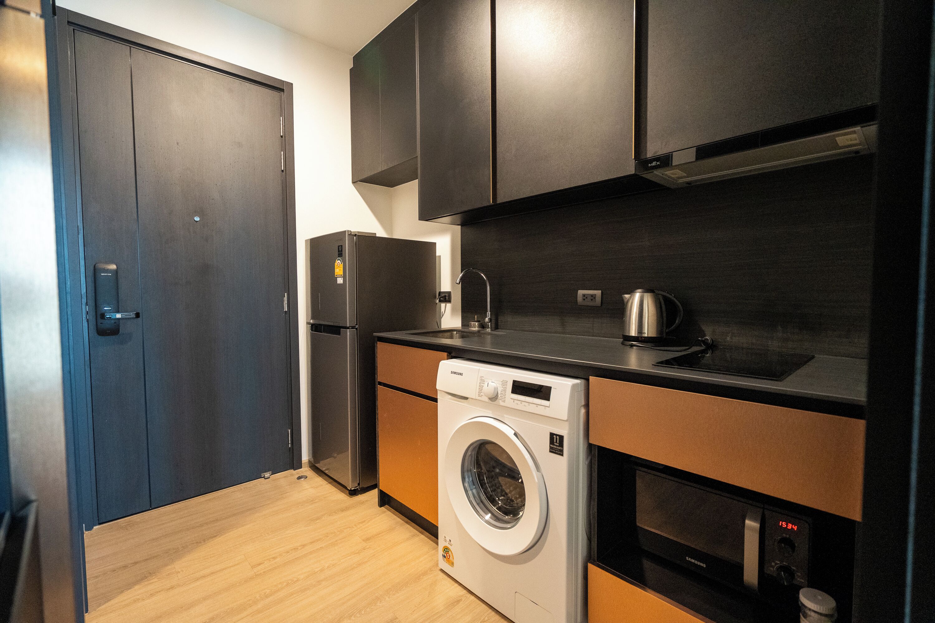 A compact kitchen with a washing machine, a refrigerator, and dark cabinetry.