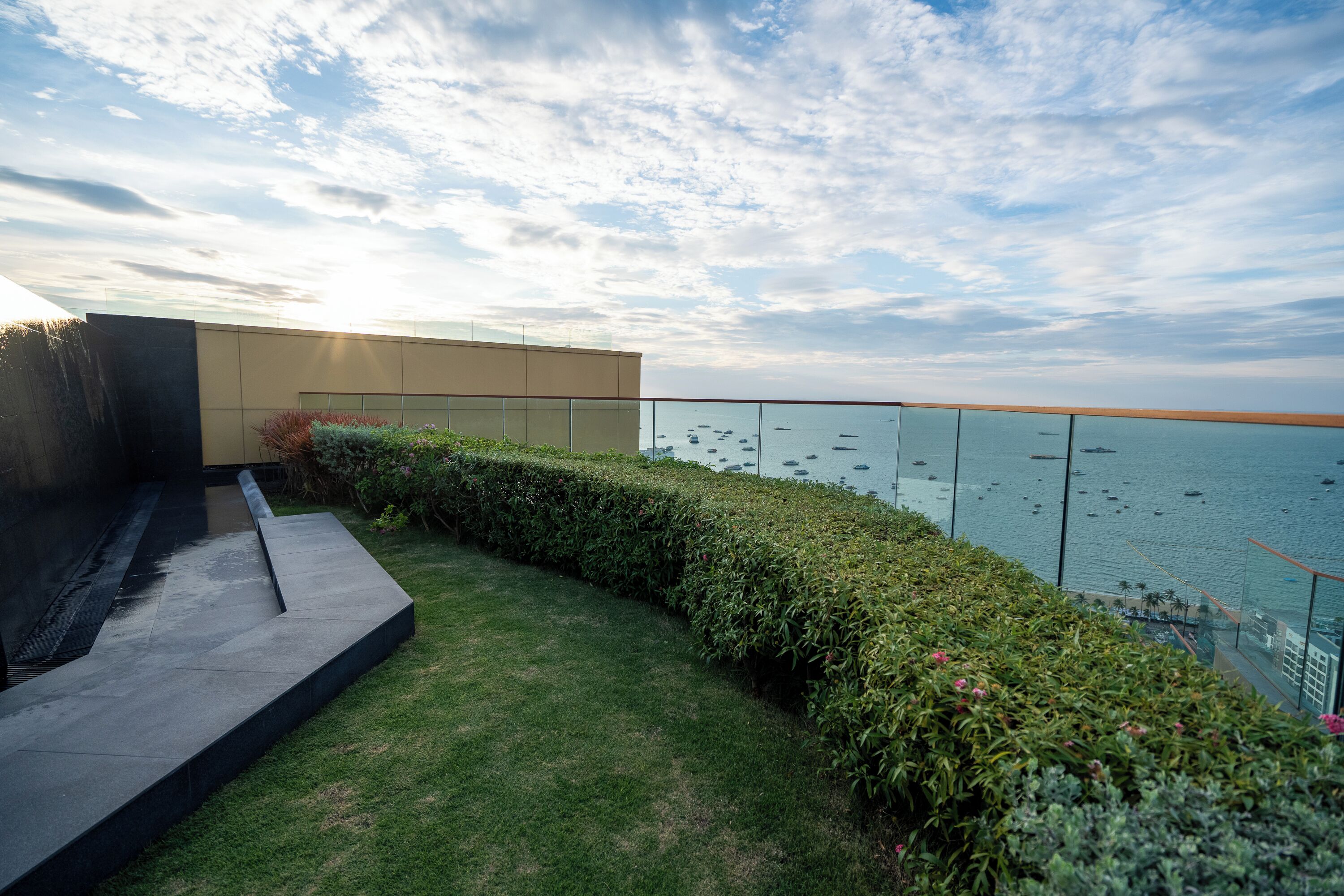 A rooftop terrace with a view of the sea, a modern building, and a glass railing.