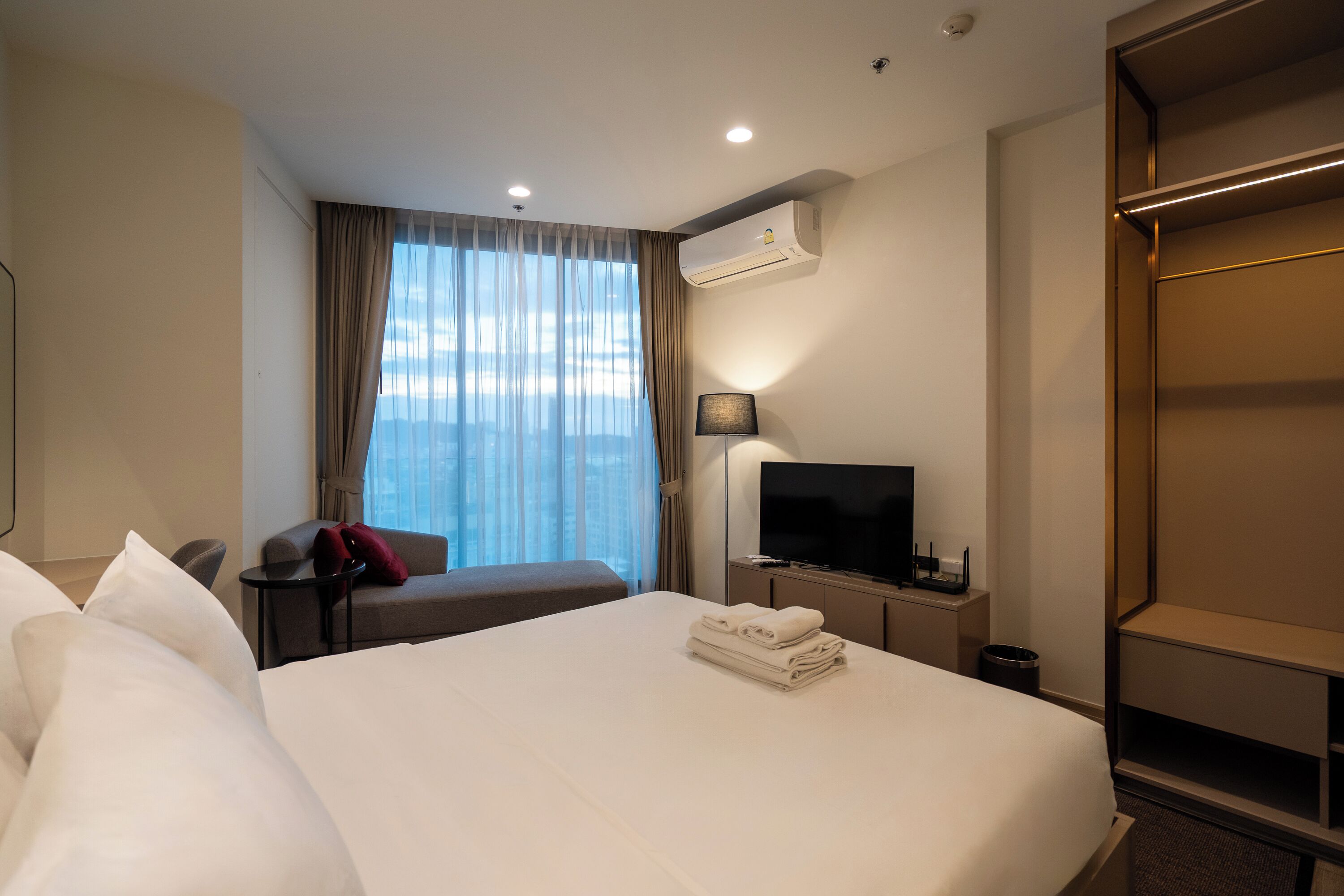 A hotel room with a large bed, a TV, a desk, and a window with curtains.