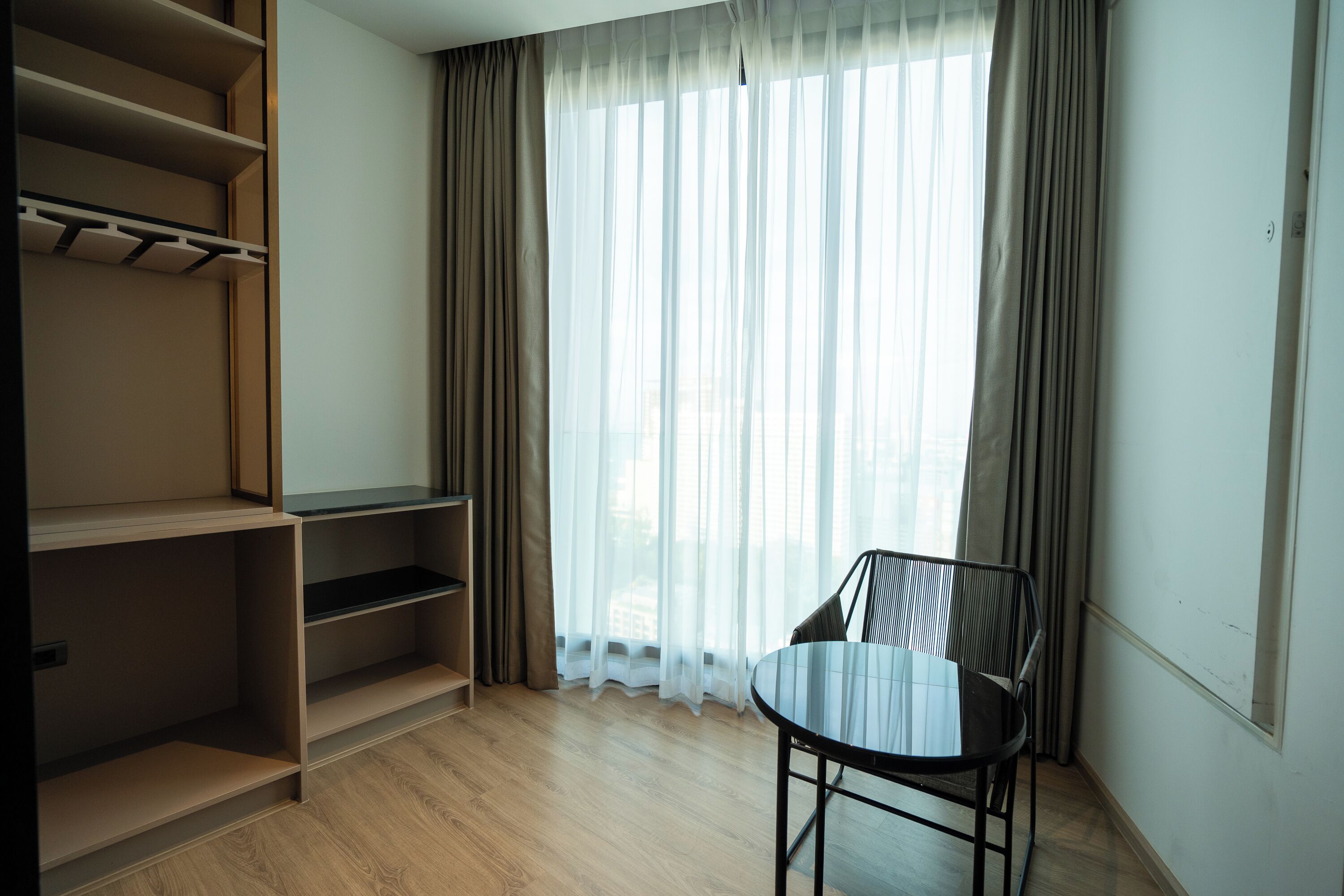 A room with a wooden floor, a black chair, a table, and a built-in shelving unit.