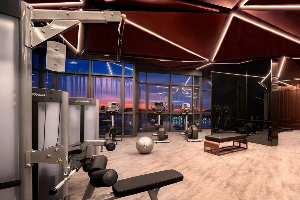 A gym with various exercise equipment, large windows, and a modern interior design.