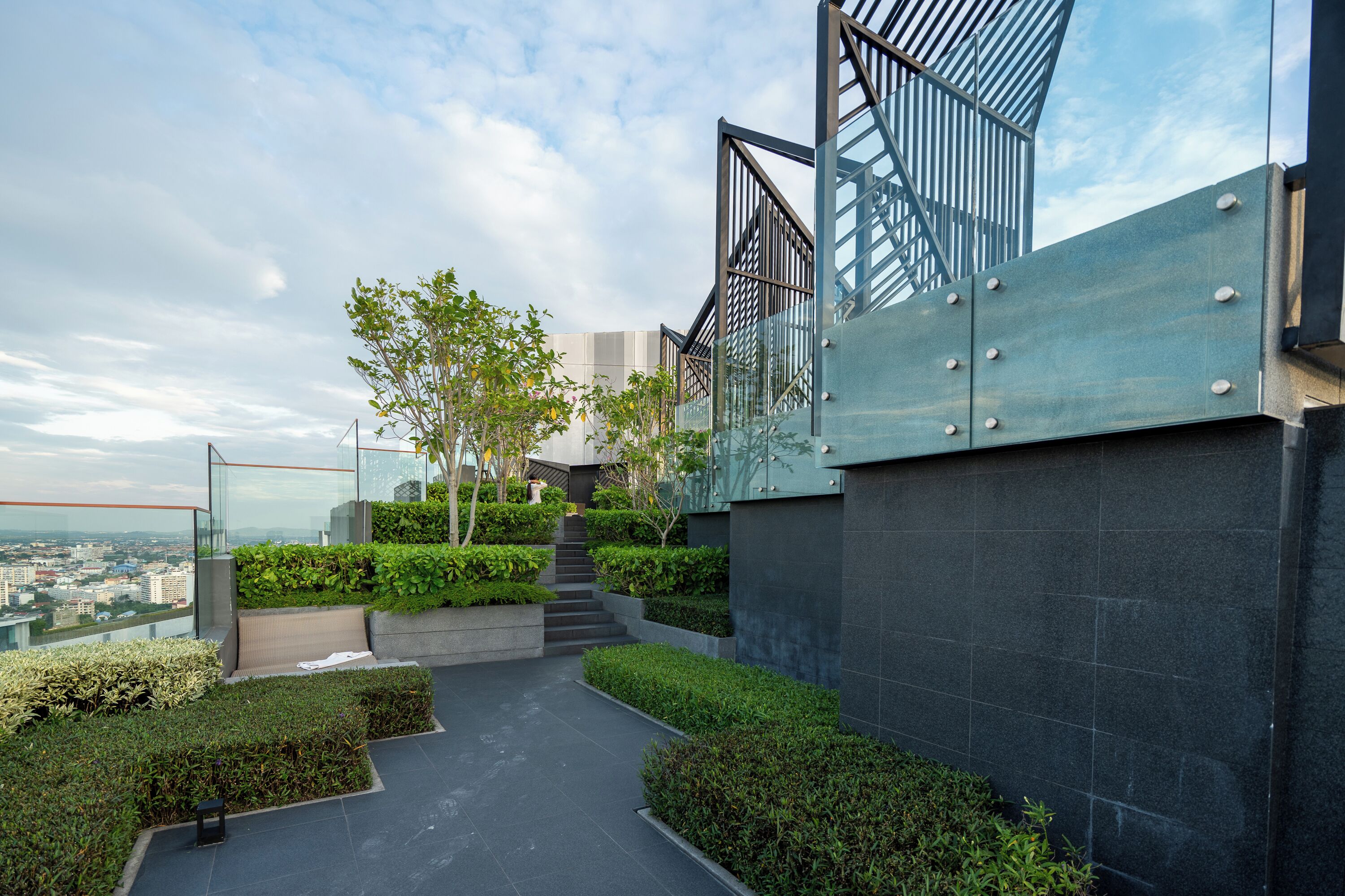 A modern building with a glass facade, a rooftop garden with steps leading to a terrace, and a view of the cityscape.