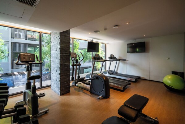 Une salle de sport moderne équipée de tapis de course, de vélos elliptiques et de poids libres, dotée de grandes fenêtres et d’un mur d’accent en pierre.