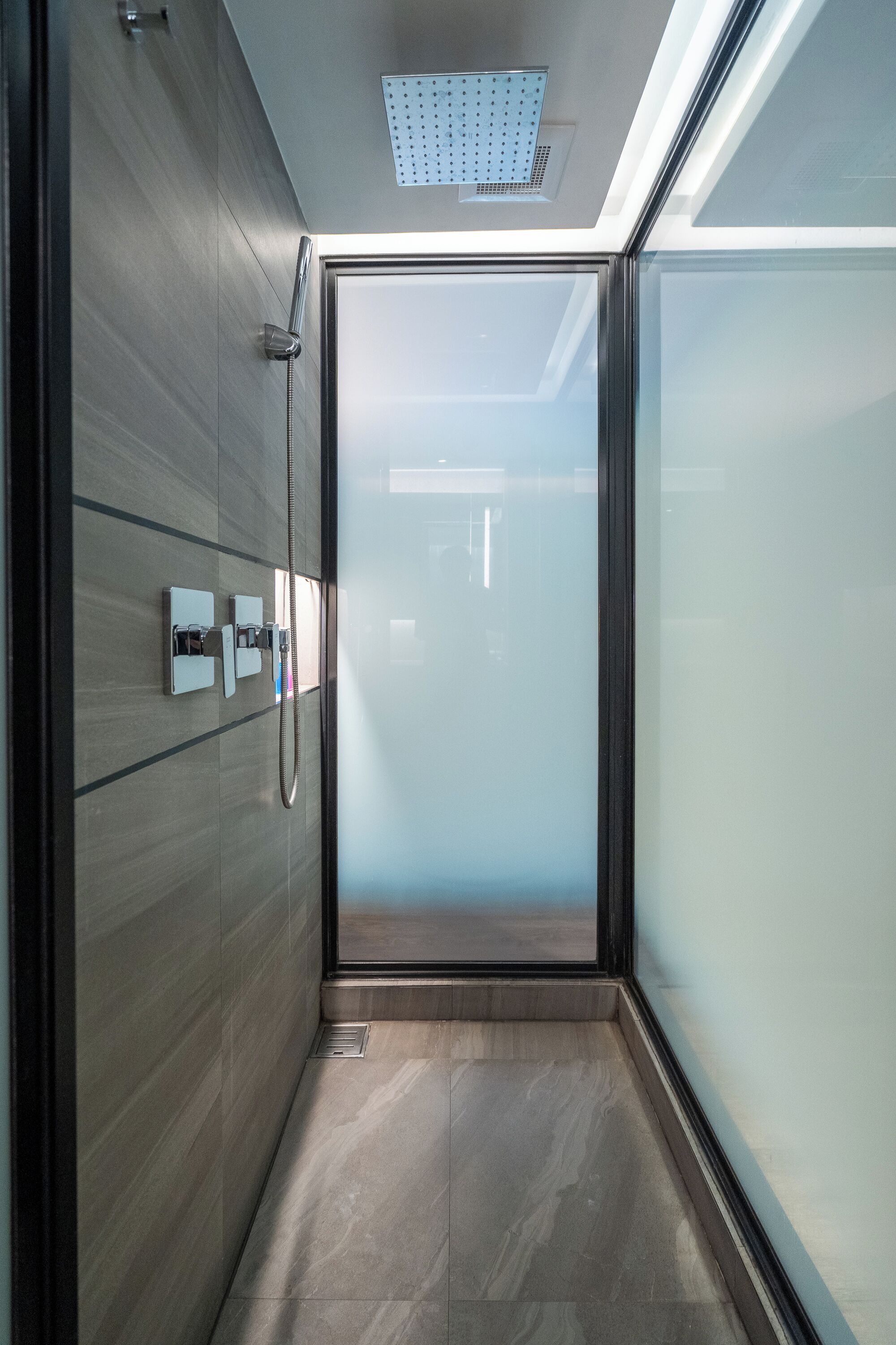 A modern bathroom with a glass shower enclosure, a visible showerhead, and a control panel for water temperature and flow.
