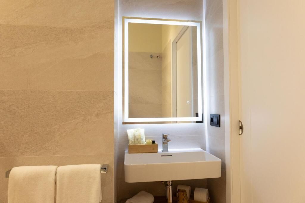 A bathroom with a white sink, a mirror with under-cabinet lighting, and a towel rack.